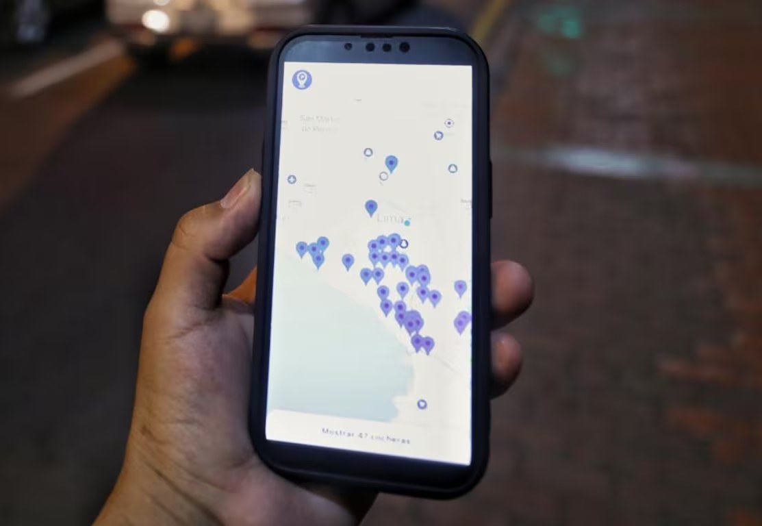 Persona sosteniendo un celular con la app de ParkGO mostrando cocheras disponibles en un mapa de Lima, de noche